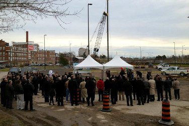 Groundbreaking ceremony on a downtown St. Catharines site, with a crane, tents and a large crowd of attendees